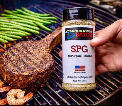 Hand holding a jar of Smokehouse Bayou seasoning over a grill with cooked food.