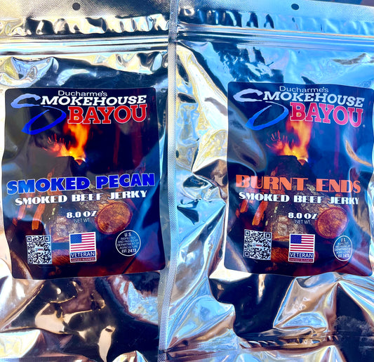 Two packages of Ducharme's Smokehouse Bayou smoked beef jerky 
8 oz bags on a reflective surface.