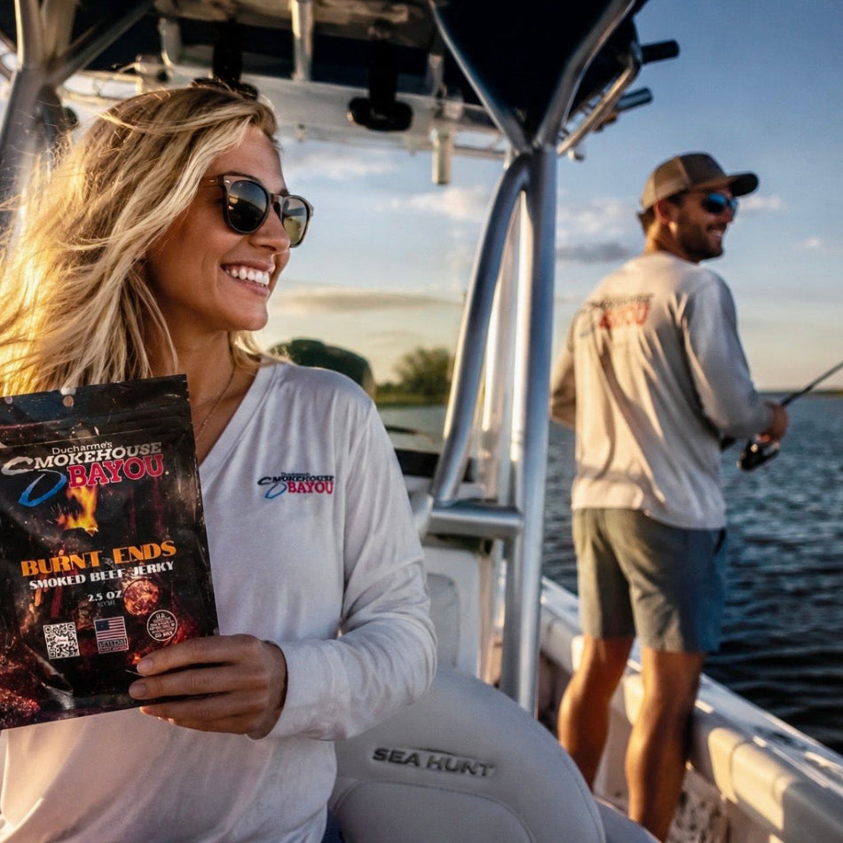 Woman on a boat holding a bag of Smokehouse Bayou Jerky , with a man fishing in the background.