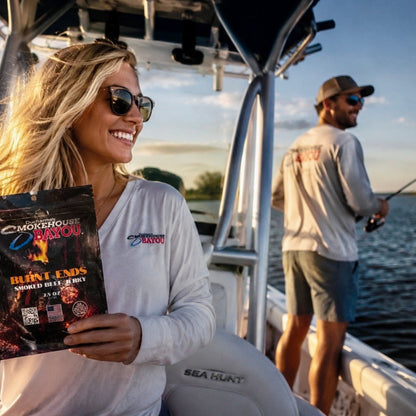 Woman on a boat holding a bag of Smokehouse Bayou Jerky , with a man fishing in the background.